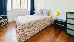 Un dormitorio con cama, una silla, un tocador y una lámpara.