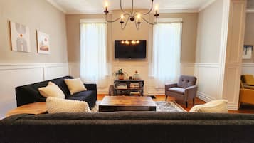A living room with a black sofa, a grey armchair, a wooden coffee table, and a chandelier.