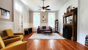 A living room with hardwood flooring, a sofa, a yellow armchair, a ceiling fan, and a fireplace.
