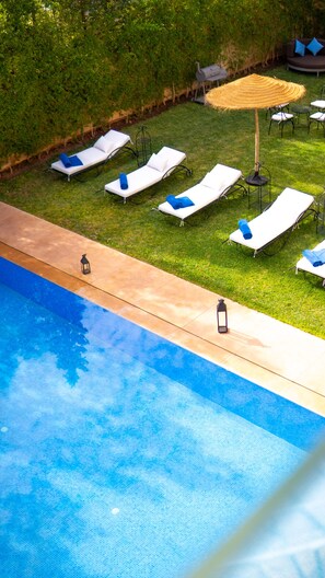 A poolside area with lounge chairs and a small table, surrounded by a grassy lawn and a hedge.