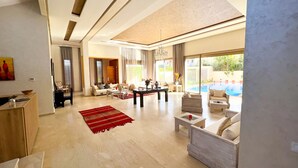 A spacious living area with a pool view, modern furniture, and a large window. - Riad villa saphir & SPA (Marrakech)