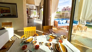 A dining area with a table set for two, a view of a swimming pool, and a glimpse of the outdoor seating area. - Riad villa saphir & SPA (Marrakech)
