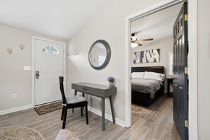 Un dormitorio con escritorio, silla, cama y una puerta que da a otra habitación.
