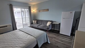 Une chambre d’hôtel comprenant un lit, un canapé, une petite table, un réfrigérateur et une porte-fenêtre coulissante donnant sur le balcon.