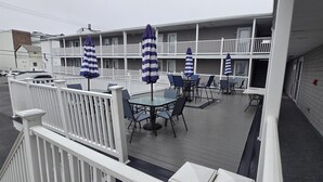 Un hôtel doté d’un balcon aménagé avec des tables et des chaises, des parasols à rayures et une clôture blanche.