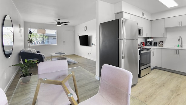 A modern kitchen with white cabinets, stainless steel appliances, and a dining area with a glass table and chairs. - Contemporary Condo in Central Biltmore (Phoenix)
