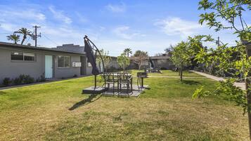 A backyard with a patio table and chairs, a small garden, and a house with a garage.