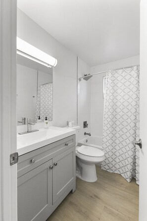 A modern bathroom with a white vanity, a large mirror, a shower, and a toilet. - Contemporary Condo in Central Biltmore (Phoenix)