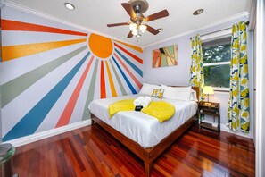 A bedroom with a wooden bed, a ceiling fan, a window with curtains, and a wall mural.