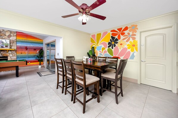 Un comedor con mesa y sillas de madera, un ventilador de techo y un mural de pared colorido.