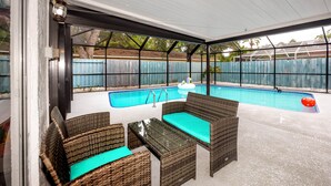 Un patio techado con piscina, mobiliario de mimbre y vistas al jardín trasero.