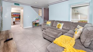 Una sala de estar con un sofá gris, una manta amarilla y una escalera que conduce a otra habitación.