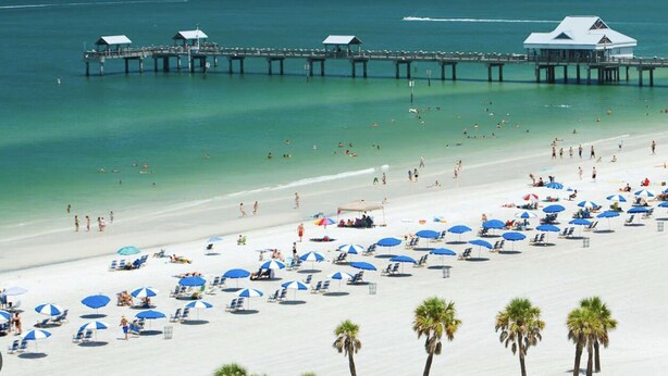 Una playa con muelle, sombrillas y palmeras.