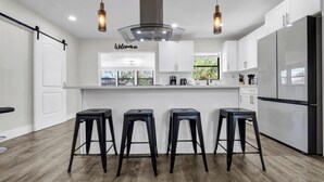 Una cocina moderna con una isla central, tres taburetes negros, armarios blancos y un refrigerador negro.