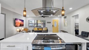 Una cocina moderna con una isla central, horno empotrado y microondas. Hay un área de comedor con un sofá y una televisión.