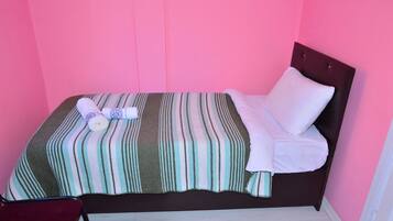 A single bed with a striped bedspread, a white pillow, and a rolled towel.