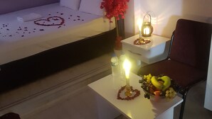A hotel room with a bed, a nightstand, a chair, a table with a candle and fruit, and a wall-mounted lamp. - Derya Otel (Borcka)