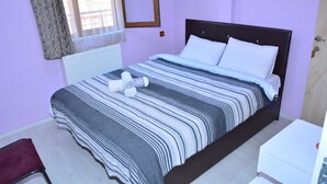 A neatly made bed with striped bedding, a white bedside table, and a window with sheer curtains. - Derya Otel (Borcka)