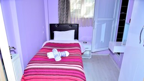 A single bed with a striped bedspread and two pillows, a nightstand with a lamp, and a window with curtains. - Derya Otel (Borcka)