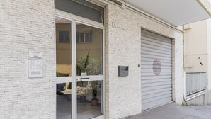 A building with a white brick facade, a glass door entrance, a garage door, and a small sign indicating 'Studio Apartments.' - GuestHost - Comfortable two-room apartment perfect for 4 guests, it is ideal for a family or small groups of friends for a relaxing holiday. We are a few minutes walk from the sea, the city center and the train station. The accommodation is equipped with (Sanremo)