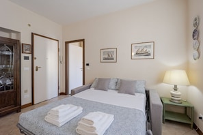 Habitación de hotel con cama, mesita de noche con lámpara, puerta y cuadros en la pared.