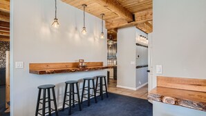 A kitchen with a wooden bar counter, four black stools, hanging pendant lights, and a stone wall. - Mountain Retreat | Fast Internet | Full Kitchen (Heber City)
