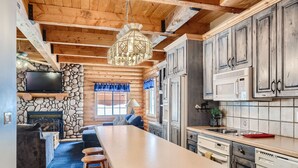 A log cabin interior with a stone fireplace, wooden ceiling beams, a large kitchen island, and built-in cabinets. - Mountain Retreat | Fast Internet | Full Kitchen (Heber City)