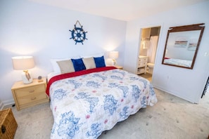 A bedroom with a bed, bedside lamps, a wall clock, a mirror, and a door leading to another room.