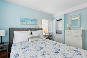 Une chambre à coucher comprenant un lit, une table de chevet, une commode, un miroir et une fenêtre avec des stores.