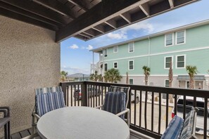 Un balcon avec une table ronde et deux chaises, donnant sur une rue où sont garées des voitures et sur un immeuble dont le revêtement extérieur est vert.