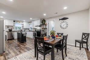 A modern kitchen with white cabinets, a dining area with a wooden table and chairs, and a clock on the wall. - Ultimate Space for Your Family! ~ TIEC ~ Fire Pit+ (Landrum)