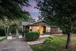 A two-story house with a front porch, a small garden, and a visible garage. - Ultimate Space for Your Family! ~ TIEC ~ Fire Pit+ (Landrum)