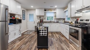 A modern kitchen with white cabinets, stainless steel appliances, and a wooden floor. - Ultimate Space for Your Family! ~ TIEC ~ Fire Pit+ (Landrum)