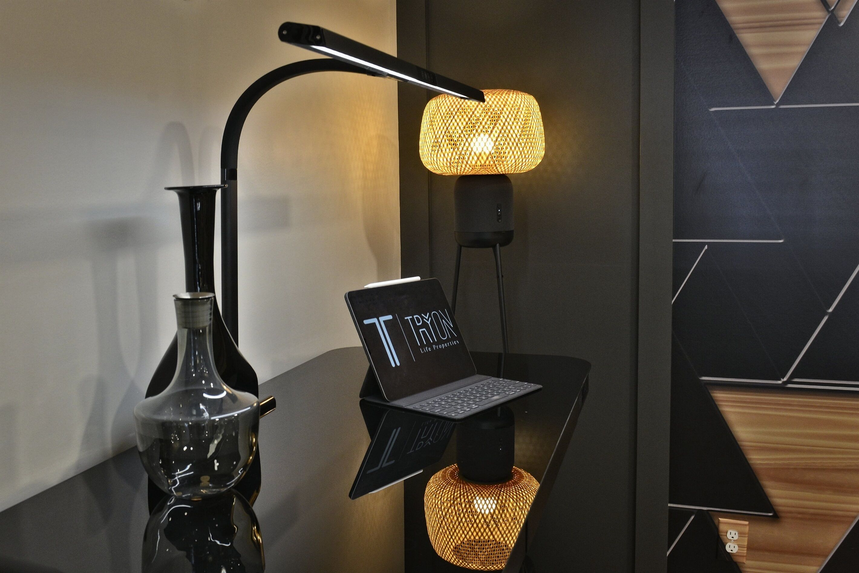 A modern lamp with a laptop on a stand, a decorative vase, and a geometric wall design.