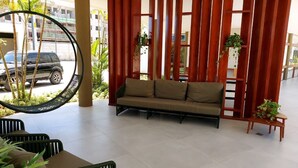 Un espacio exterior moderno con asientos, incluyendo un sofá, sillas y una mecedora, además de un separador de madera con plantas.