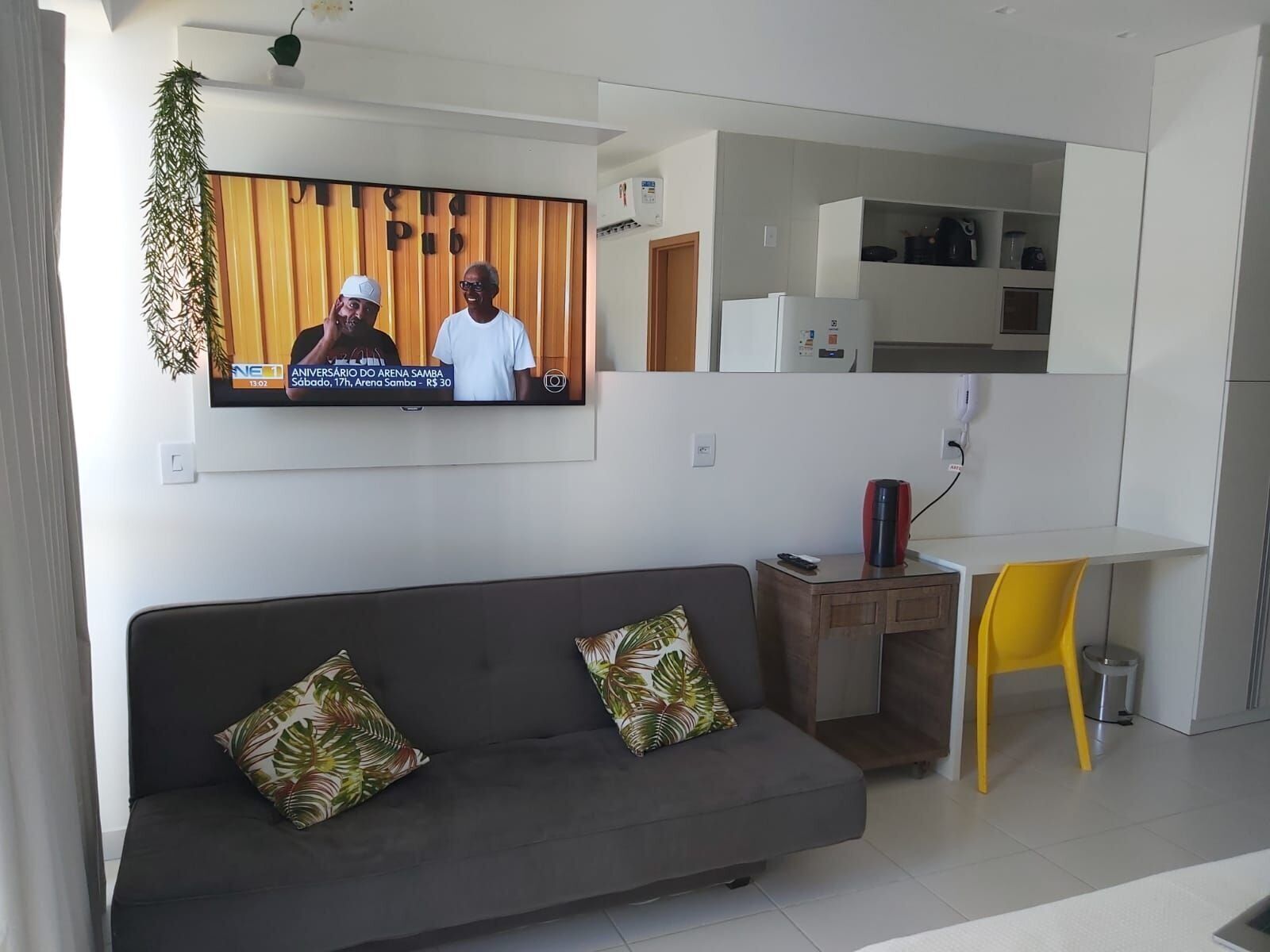 A modern living room with a grey sofa, yellow chair, and a TV displaying a news broadcast.
