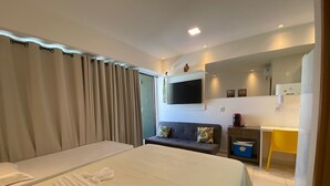 Habitación de hotel con una cama grande, un sofá, un televisor montado en la pared, una mesita y un área de baño con inodoro y lavabo.