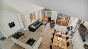 Une cuisine moderne dotée d’un îlot central, d’un coin repas avec des tables rondes et d’un salon avec un canapé et des fauteuils.