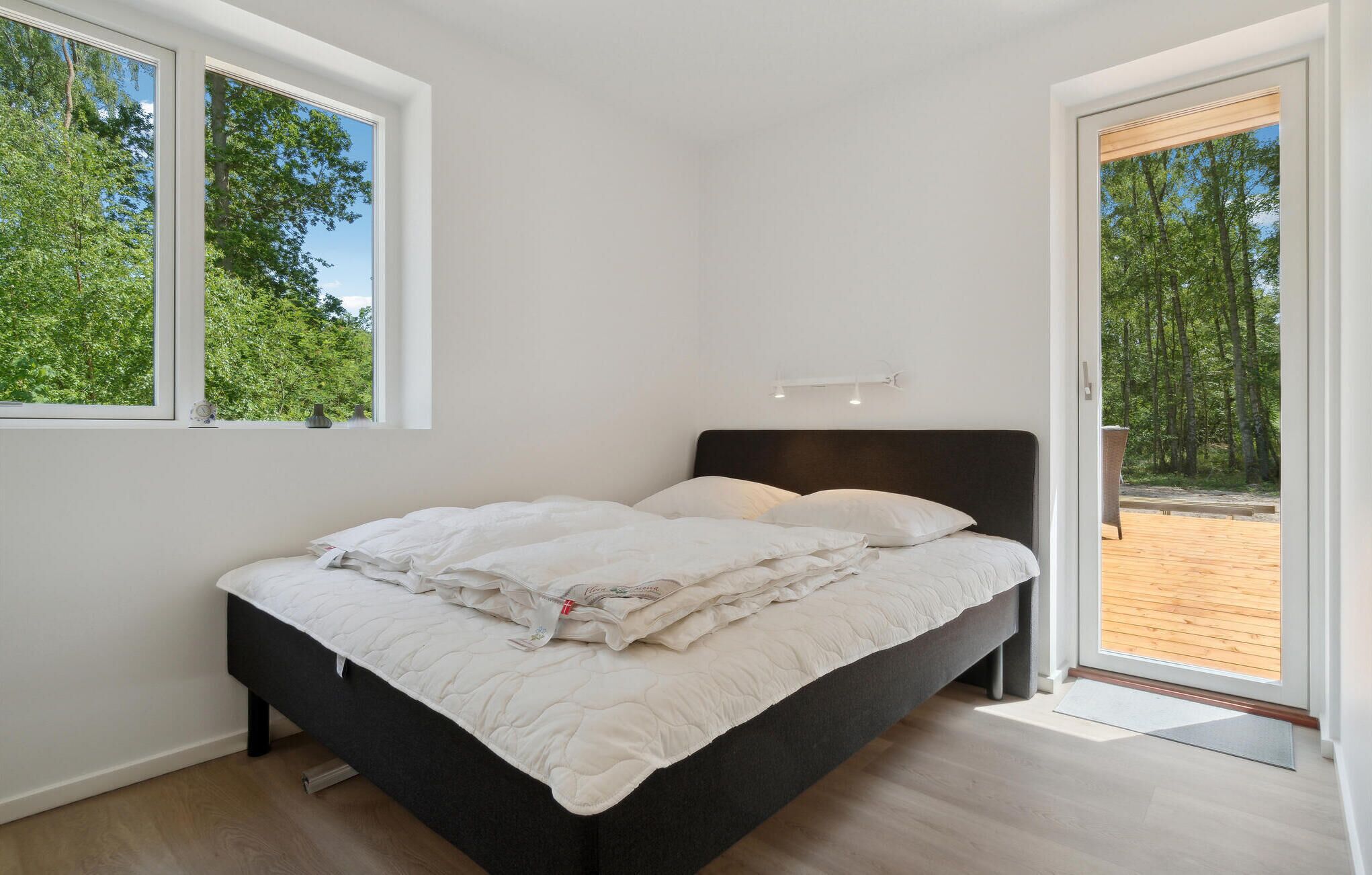 Ein Schlafzimmer mit einem Bett, zwei Fenstern und Blick auf eine Holzterrasse.