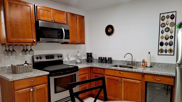 A kitchen with wooden cabinets, a stainless steel microwave, a stove, a sink, and a marble countertop. - New, Cozy & peaceful stay, 30 minutes from New Orleans. Family and pet friendly! (Slidell)
