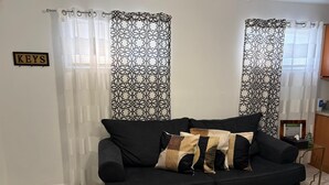 A black sofa with patterned cushions, a sign labeled "KEYS" on the wall, and patterned curtains. - New, Cozy & peaceful stay, 30 minutes from New Orleans. Family and pet friendly! (Slidell)