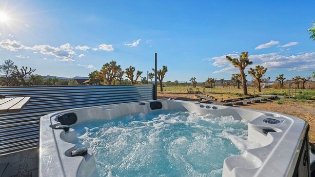 A hot tub with a clear view of a desert landscape, including Joshua trees and a wooden deck.