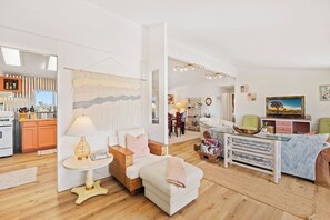 A modern living room with a sofa, a coffee table, and a TV. There is a kitchen area with a stove and cabinets.