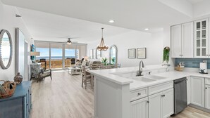 Une cuisine moderne dotée d’un grand îlot central, de meubles blancs et offrant une vue sur l’extérieur.