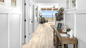 Un couloir doté d’un plancher en bois, de murs blancs et d’œuvres d’art encadrées. On y trouve un banc en bois sur lequel est posé un vase, ainsi qu’une petite table sur laquelle se trouvent un tableau encadré et un panneau.