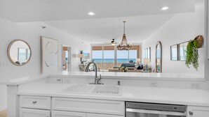 Une cuisine moderne avec des meubles blancs, un lave-vaisselle intégré et une grande fenêtre donnant sur la plage.