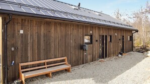 Una construcción de madera con techo de metal, un banco y un camino de grava.