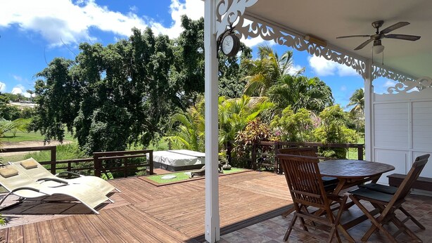 A wooden deck with a table and chairs, a covered seating area, and a view of greenery. - Zen Fairway Apartment Nestled in the heart of the golf course (Saint-François)