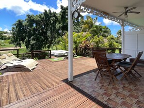 Eine Holzterrasse mit Tisch und Stühlen, ein überdachter Sitzbereich und Blick ins Grüne.