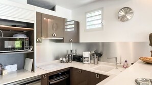 A modern kitchen with a microwave, oven, and coffee maker. There are cabinets, a sink, and a clock on the wall. - Zen Fairway Apartment Nestled in the heart of the golf course (Saint-François)
